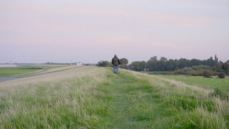 Person-walking-on-green-and-yellow-dyke-or-dam-near-north-sea,-lower-saxony,-Germany-4K