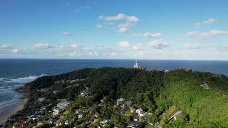 byron bay, nsw, showcasing lush greenery, coastal cliffs, and a distant lighthouse, aerial view