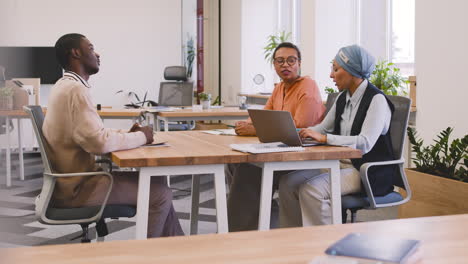 An-Woman-And-A-Muslim-Woman-Co-Workers-Interview-A-Young-Man-Sitting-At-A-Table-In-The-Office-16