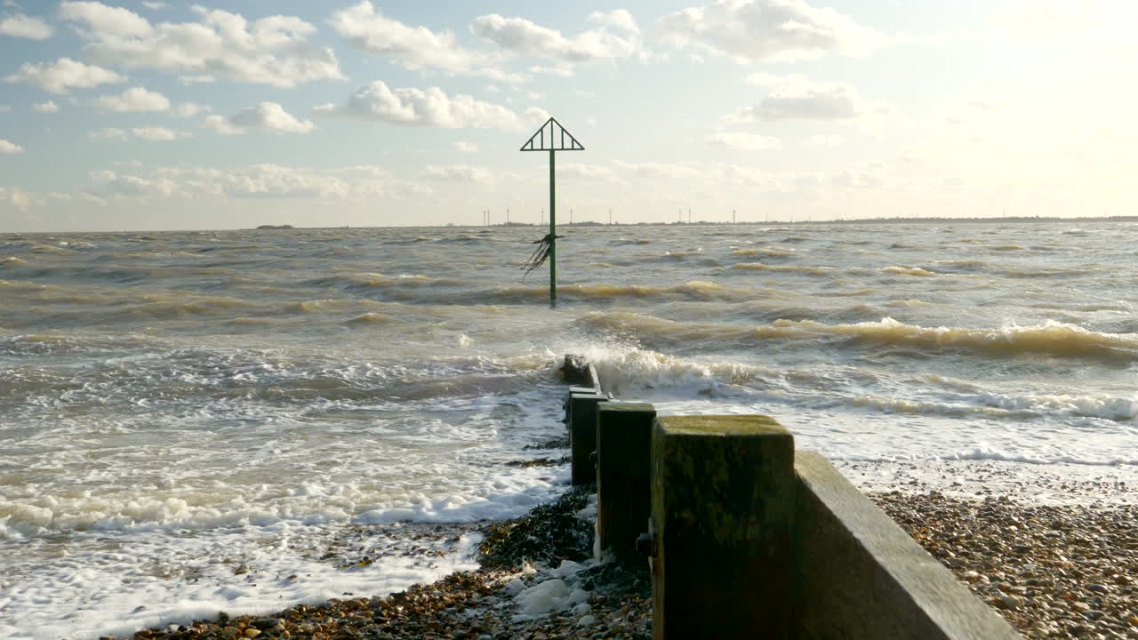 Waves crashing on a pebble beach with a navigation marker
