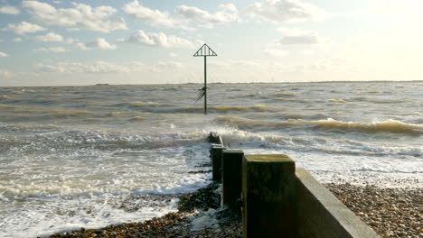 waves crashing on a pebble beach with a navigation marker