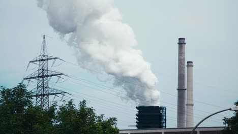 Plano-Cinematográfico-Amplio-De-Una-Planta-De-Energía,-Humo-Subiendo,-Filmado-Con-árboles-En-Primer-Plano