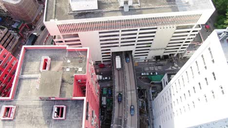 Traffic-passing-through-a-Car-park-building-in-downtown-Hong-Kong,-with-city-mega-buildings,-Aerial-view