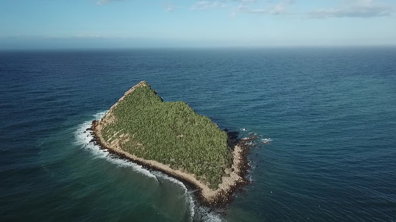 Cinematic aerial drone shot of a solitary rock island floating in the deep blue open Mediterranean waters. A minimalist nature seascape view