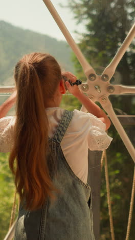 child with camera takes records at glamping. little girl shoots wild landscape with videocamera through glass wall. kid plays on family holiday