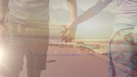 sección media de una pareja caucásica caminando de la mano junto al mar, sobre las nubes