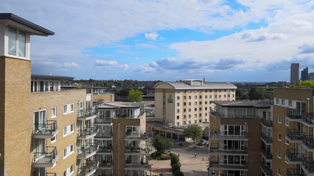 Drone footage of Royal Arsenal Riverside in Woolwich, London, England, featuring modern apartment buildings, landscaped walkway, and central courtyard under bright sky, highlighting urban design