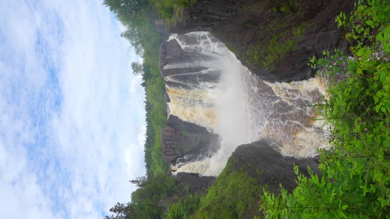 Landscape video of a foaming waterfall falling into the river and the blue sky
