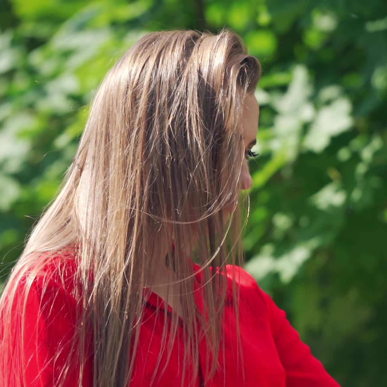 Attractive model with a mobile phone outdoors. Beautiful woman doing selfie in the street on green tree background. Lovely girl is recording video of herself on a phone.