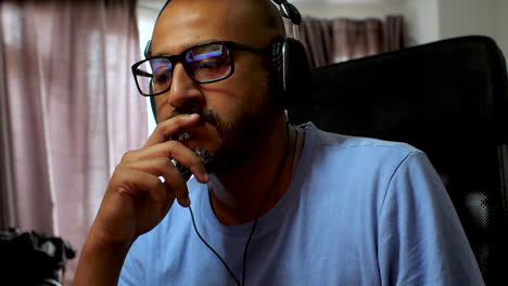 Man-is-listening-to-music-with-headphones-at-his-home-office,-deep-in-thought