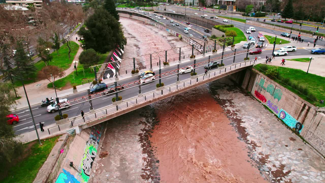 Fly over a bridge connecting the city of Santiago Chile with the brown colored Mapocho river and high vehicular flow