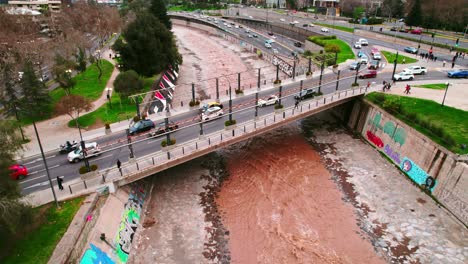 Sobrevolar-Un-Puente-Que-Conecta-La-Ciudad-De-Santiago-Chile-Con-El-Río-Mapocho-De-Color-Marrón-Y-Alto-Flujo-Vehicular