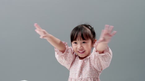 드레스를 입고 웃고 손을 흔들며 스튜디오에서 카메라를 바라보는 작은 아시아 소녀