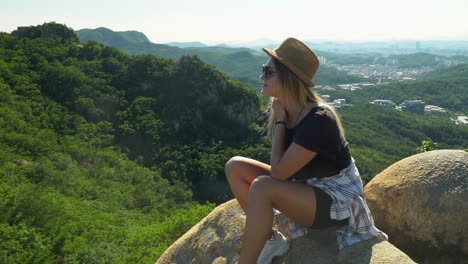 Stilvolles-Mädchen,-Das-Auf-Den-Felsen-Sitzt-Und-Den-üppigen-Wald-Am-Gwanaksan-berg-An-Einem-Sonnigen-Sommertag-In-Seoul,-Südkorea,-Genießt