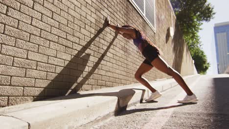 african american woman exercising outdoors leaning of wall and stretching in the city