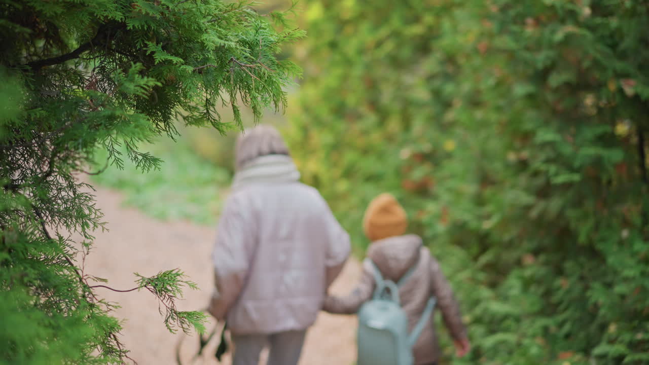 woman holds kid hand and leash walking down mossy forest steps, blurred figures visible ahead, autumn greenery surrounding staircase, warm jackets and scarf, tender guiding family