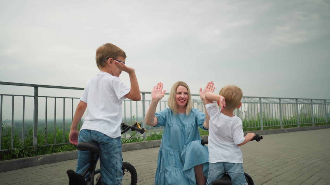 즐거운 어머니는 자전거를 타고 있는 아이들과 함께 즐거운 야외 시간을 보내며 사랑과 웃음으로 가득 찬 하이파이브를 치고 있습니다.