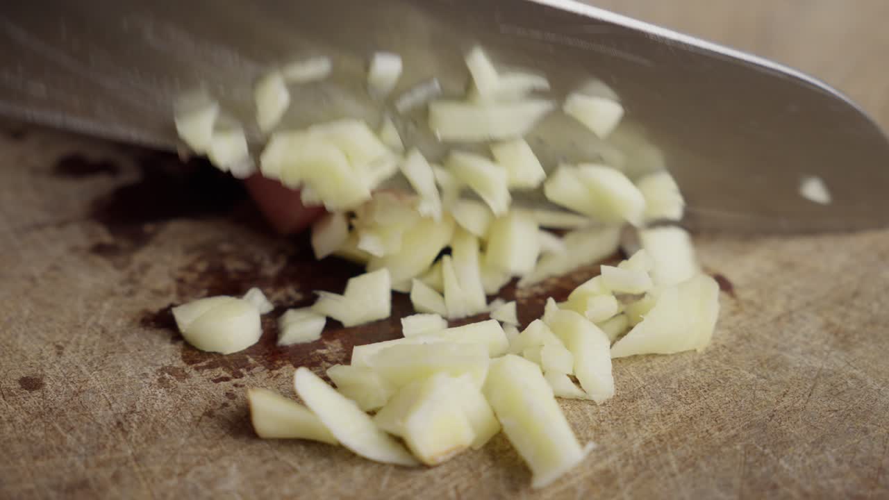 Hand chopping fresh garlic cloves on a wooden cutting board with a silver knife