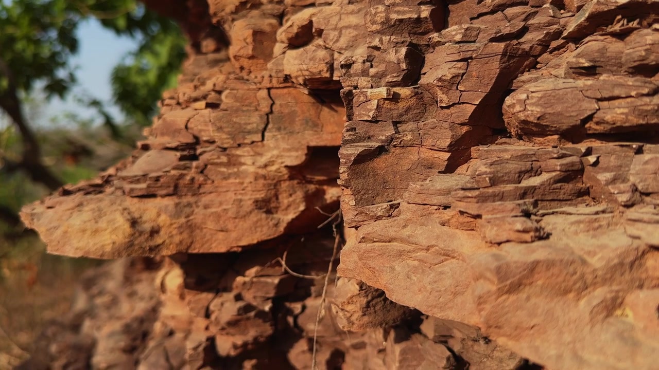 Lento movimento di jib verso il basso attraverso strati di roccia sedimentaria esposti che rivela texture geologiche alterate, fratture naturali e l'intricata struttura di una formazione rocciosa scoscesa