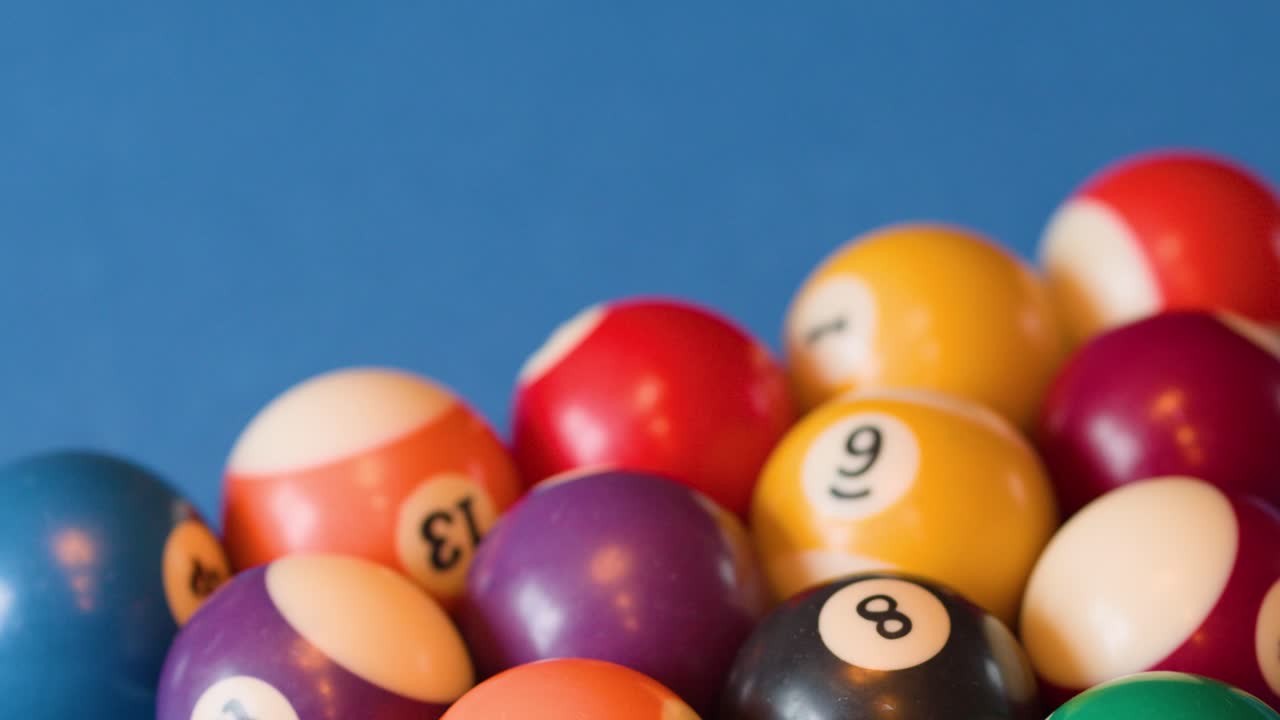 Colorful billiard balls scatter across blue felt table, natural lighting, close-up, shallow focus
