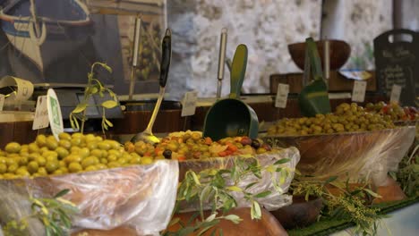 stall-of-an-outdoor-market-with-large-containers-filled-with-different-olives-with-small-shovels-to-help-themselves