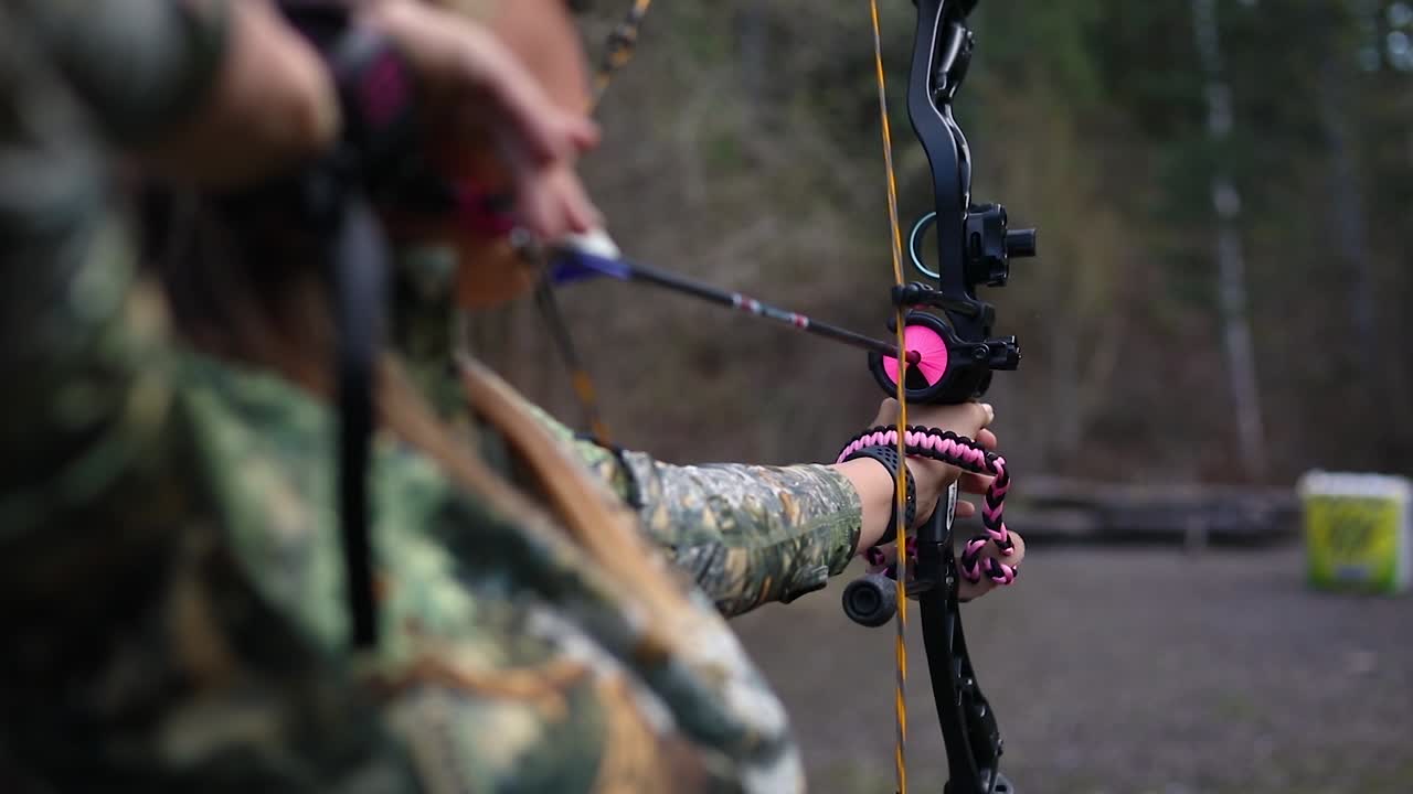 una niña sosteniendo un arco y una flecha que se tira hacia atrás y está lista para disparar al objetivo