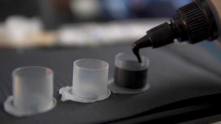 Filmagem macro detalhada de tinta preta para tatuagem sendo dispensada em batoques de tinta plásticos estéreis, destacando a preparação precisa sob luz suave de estúdio.