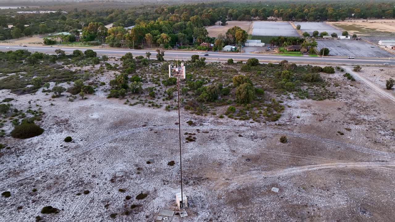 Aerial top shot of a single telecommunication tower standing tall beside a running highway at countryside.