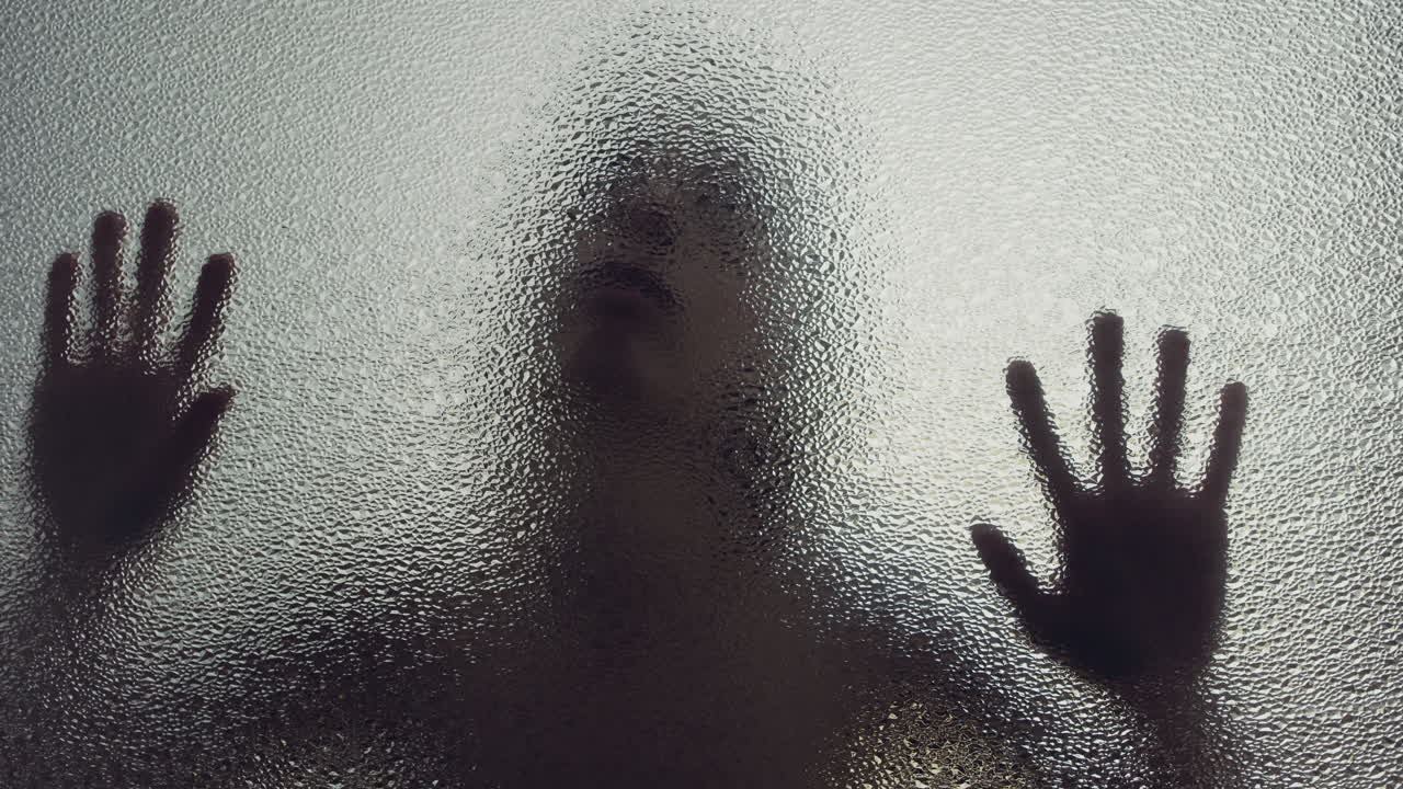 A female silhouette behind the frosted window touches the glass slowly