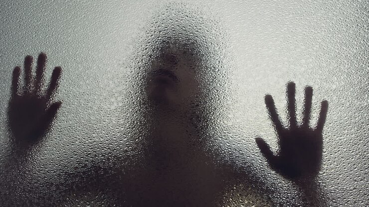 Una silhouette femminile dietro la finestra smerigliata tocca lentamente il vetro.