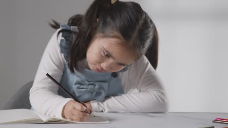 Studio-Shot-Of-Young-Girl-At-Table-Writing-In-School-Book-1