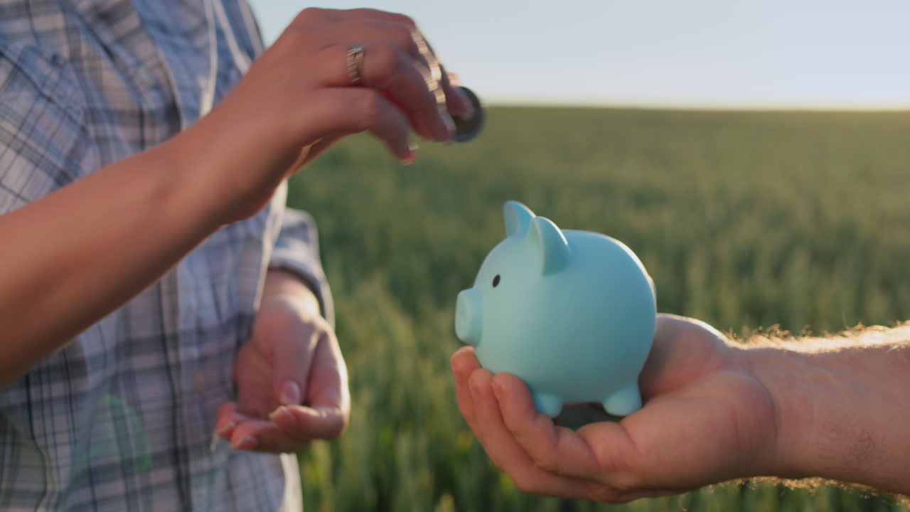 A woman's hand puts coins in a piggy bank held by her husband. Family budget concept