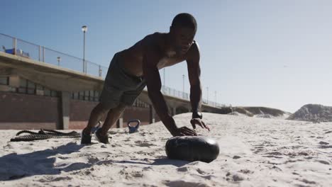 hombre afroamericano enfocado haciendo abdominales en la pelota, haciendo ejercicio al aire libre en la playa