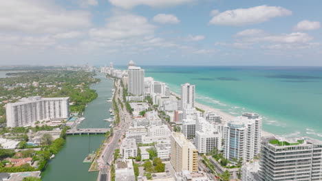 Fly-over-stripe-of-high-rise-buildings-along-sea-coast.-Traffic-on-highway-passing-through-urban-borough.-Amazing-aerial-panoramic-shot-of-tropical-destination.-Miami,-USA