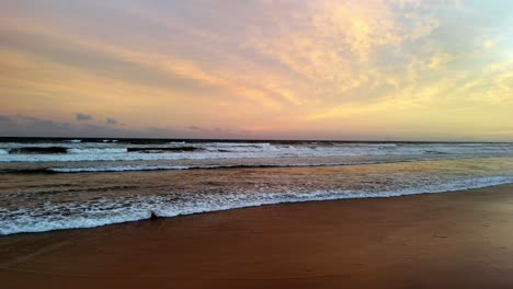 Los-Suaves-Tonos-Pastel-Del-Amanecer-Reflejándose-En-La-Playa,-Las-Olas-Bañando-Suavemente-La-Arena-Bajo-Un-Cielo-Rayado-De-Nubes