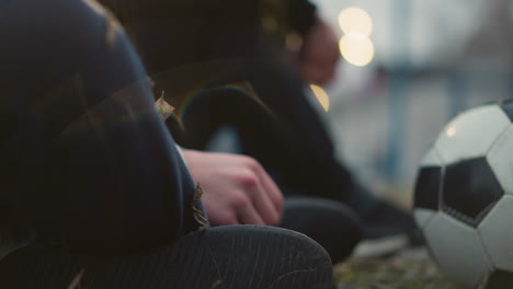 close-up of two persons seated on the grass with light reflections and grass particles on one person's leg, with a blurred background