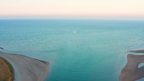 aerial drone shot flying toward the sea at sunset with boat returning to shore