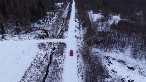 drone retreats upward as red car drives toward camera on snowy forest road