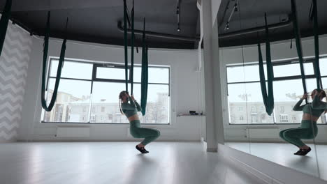 young beautiful woman practice in aero stretching swing. young woman rolls her head upside down in a hammock for aerial yoga. focused pretty mature woman doing aerial yoga in gym