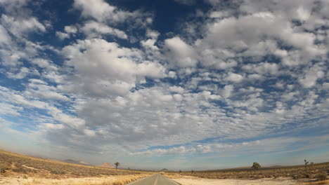 driving along a road straight through the mojave desert toward the distant mountains - point of view