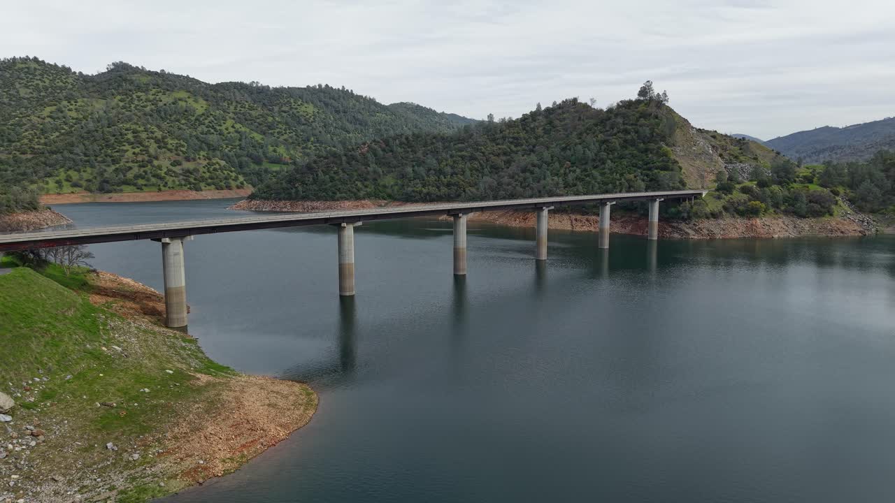 Sweeping drone views highlight the Don Pedro Reservoir Bridge, as a vehicle crosses its sturdy structure over the tranquil waters.