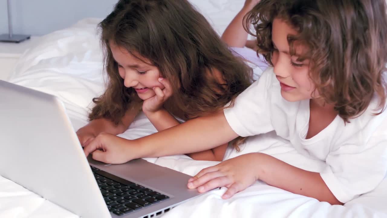 hermanos lindos usando computadora portátil en la cama de sus padres