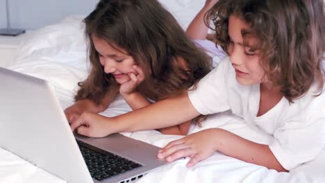 cute siblings using laptop on their parents bed