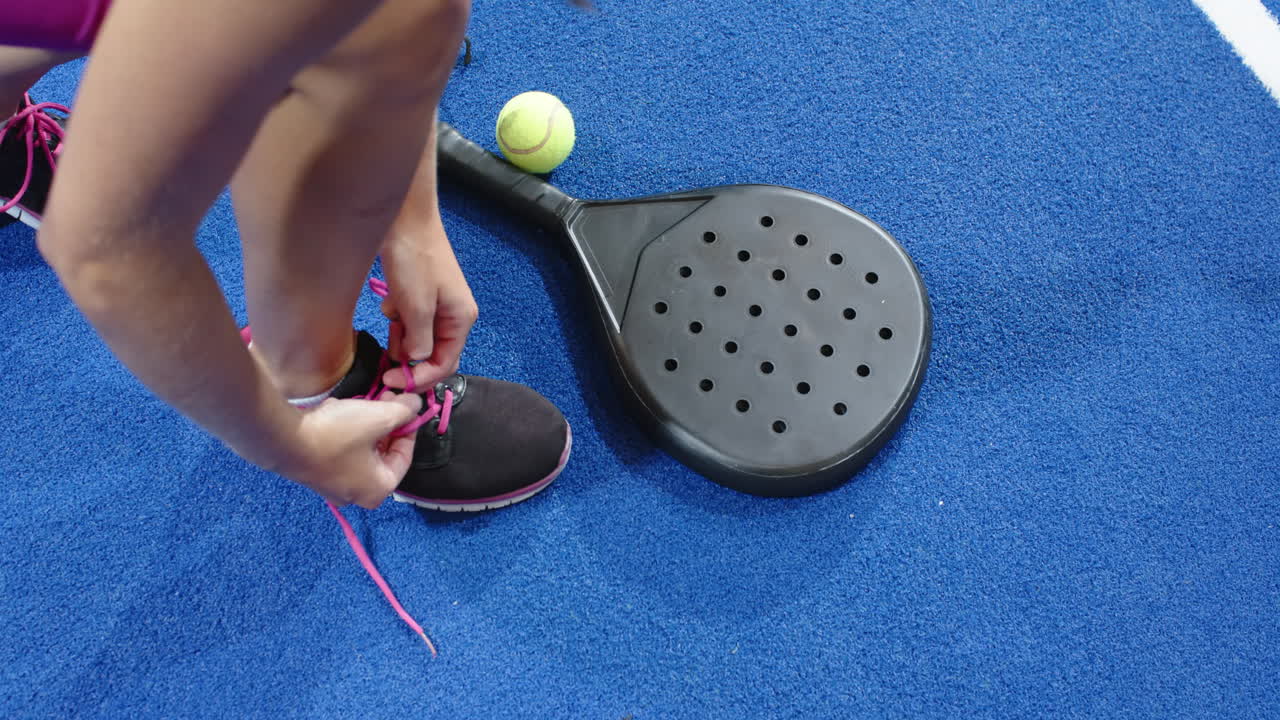 Tying shoelaces next to padel racket and ball on blue indoor court