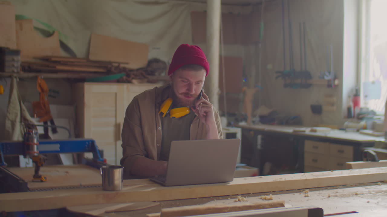 Woodworker Talking on Phone and Using Laptop in Workshop