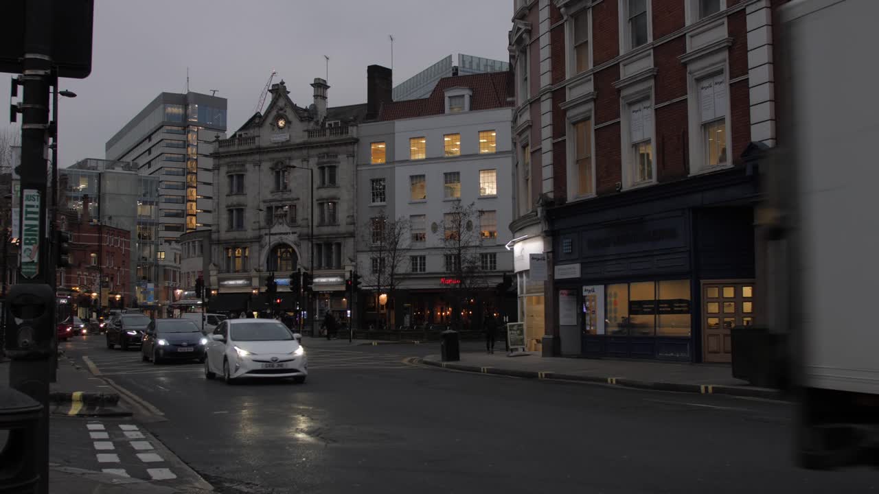 Red double-decker bus leaving Hammersmith station at dusk with city lights illuminating buildings