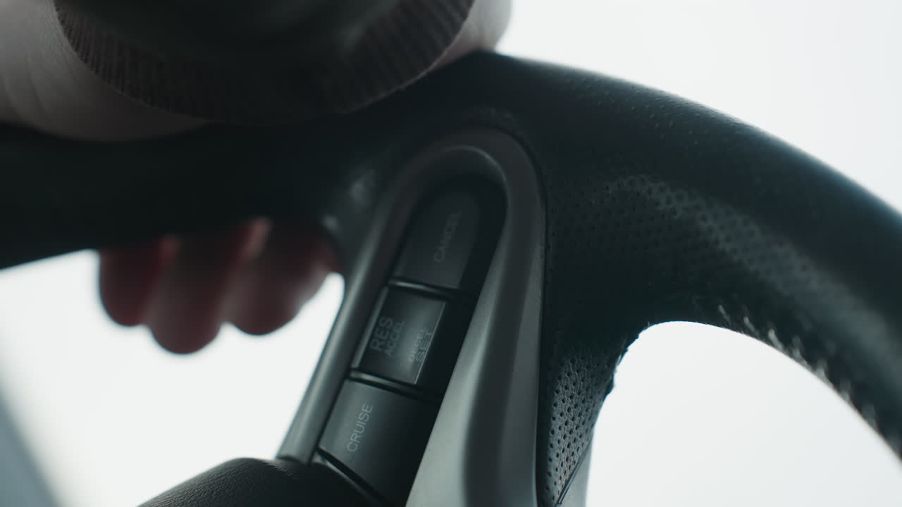 Close up of person pressing cruise control cancel button on steering wheel while holding grip of wheel showing finger interaction with control switch in modern car cabin interior