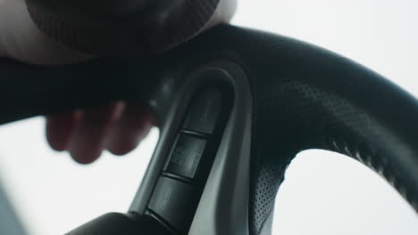 close up of person pressing cruise control cancel button on steering wheel while holding grip of wheel showing finger interaction with control switch in modern car cabin interior