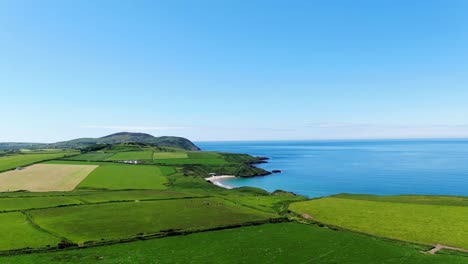 Rising-Aerial-view-of-Whistling-sands-over-green-fields-towards-the-beach-with-blue-skies-on-a-summer`s-day