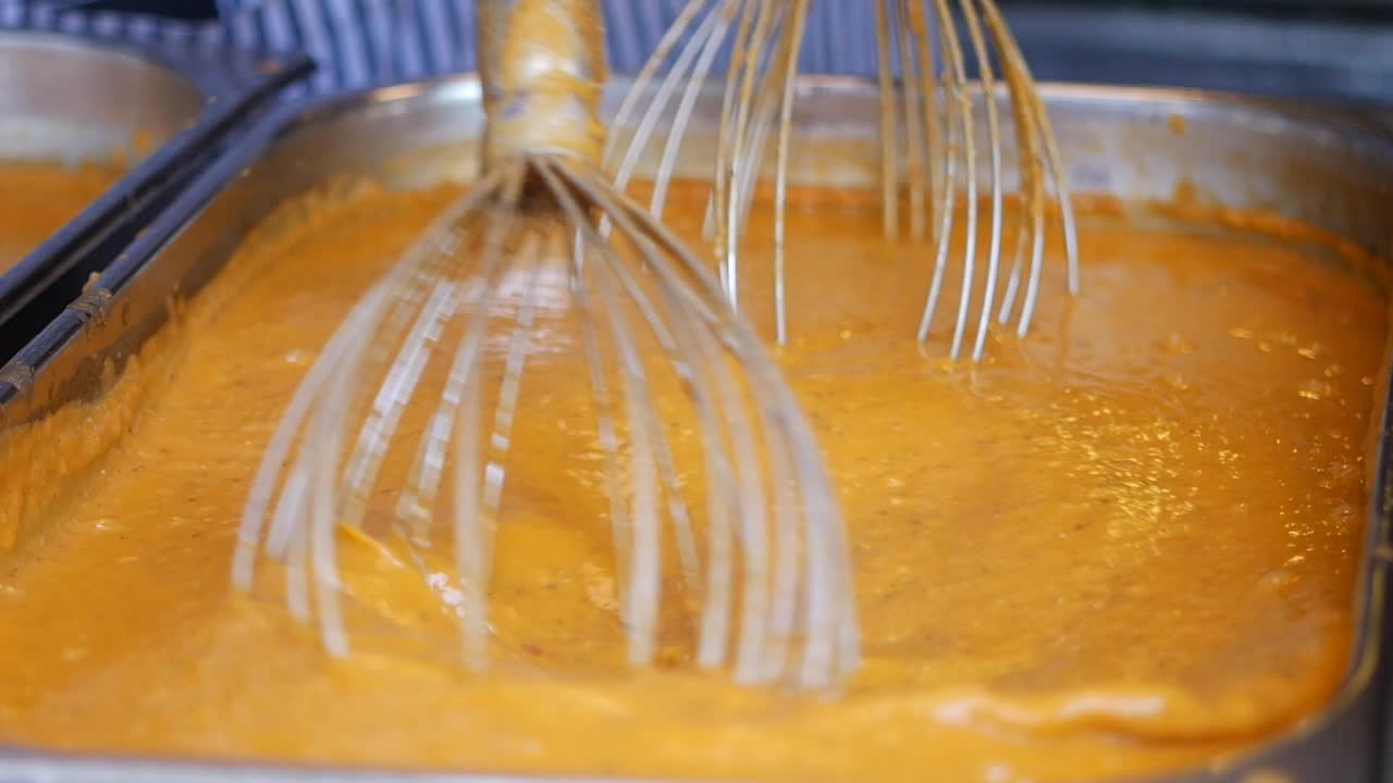 un primer plano de un batidor mezclando sopa de naranja en una sartén de metal